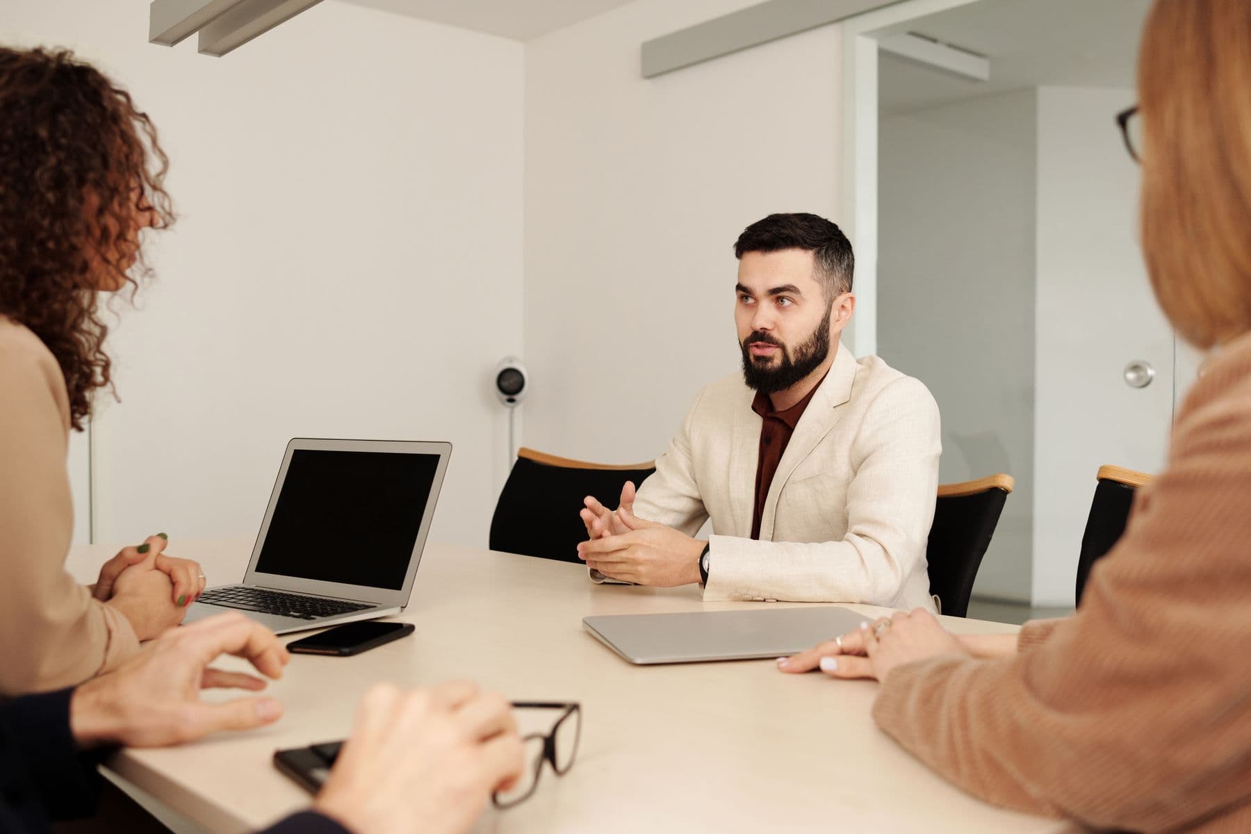 Three people talk across a table in a bright office meeting room.